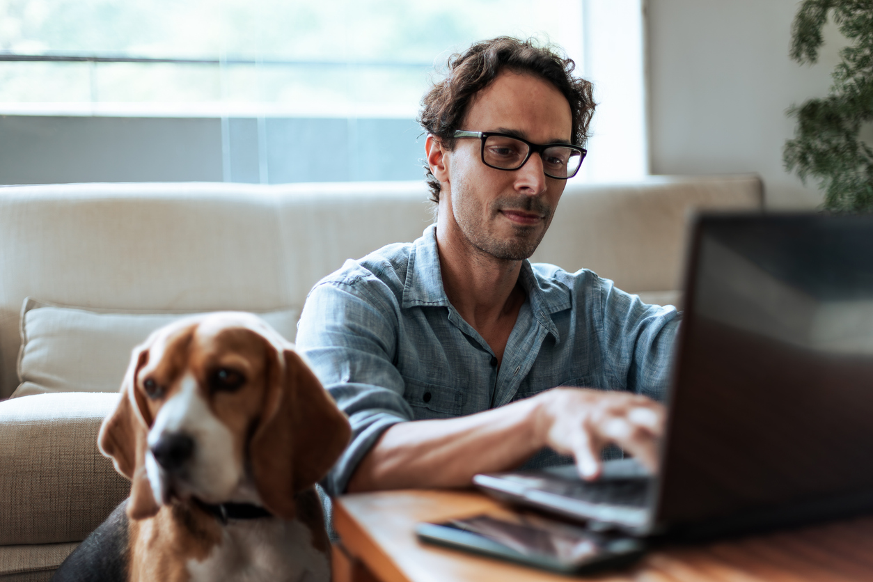 Mid aged man comfortably working at home sitting on the floor with his Beagle dog by his side